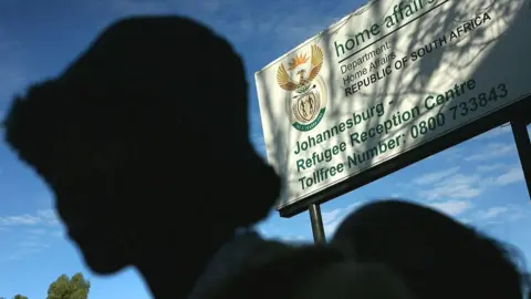 Getty Images A silhouetted figure in a hat stands in line near the entrance of a government refugee centre in Johannesburg, South Africa - archive shot