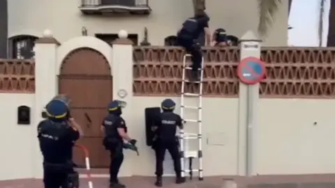 Guardia di Finanza Police climb a ladder at a villa in an undisclosed location