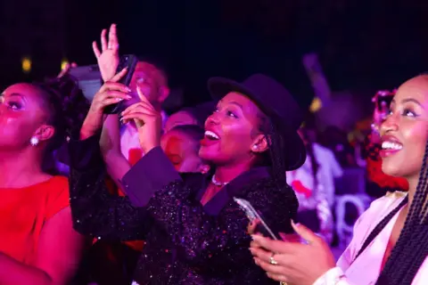 AFP via Getty Images Fans react during a concert by Fally Ipupa at the Serena Hotel in Goma, DR Congo. Some smile and wave while others film him on their phone.