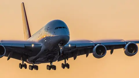 Getty Images Close up shot of Qantas aircraft in the air overhead, silhouetted against an orange sky