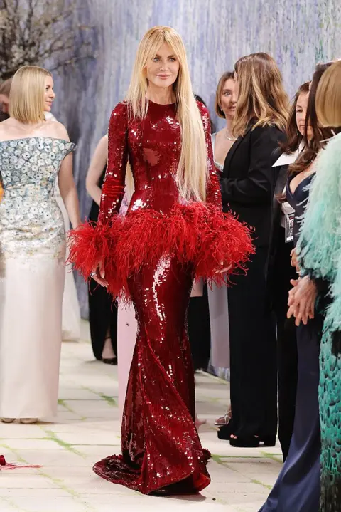 Getty Images Actress Nicole Kidman wears a long-sleeved beaded column gown in a deep red shade. Red feather ruffles adorn her sleeve cuffs and midriff.