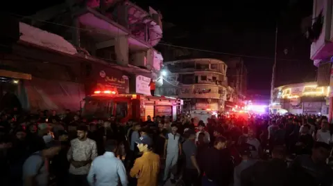 Reuters Large crowds gathered at the scene of the attack, with emergency vehicles flashing beside damaged buildings