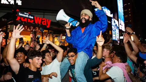 Getty Images Crowds of fans cheering and celebrating, with one fan sitting on another's shoulders and yelling into a megaphone