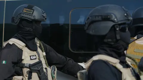 AP Photo/Sunday Alamba Two government forces personnel wearing all black and beige vests.