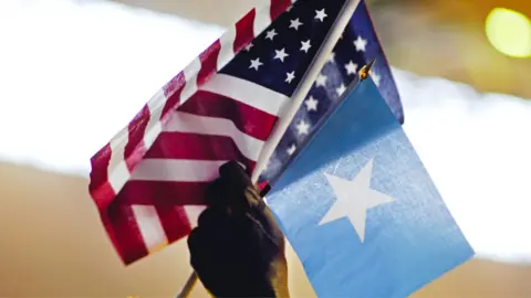 Washington Post via Getty Images A close-up of a man's holding a Somali and a US flag