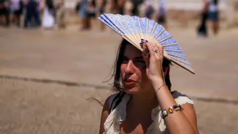 Getty Images A woman shades her head with a fan in front of Jeronimos Monastery in Belem, Portugal