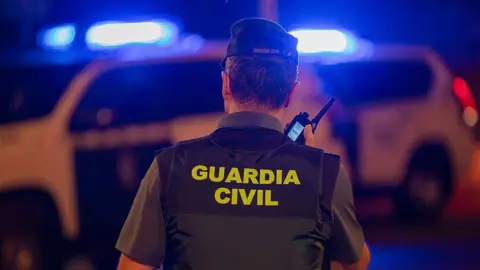 Getty Images A policeman speaks into a phone with his back turned to the camera, with 'Guardia Civil' written on the back of his vest. A police car with flashing blue lights is visible in the background.