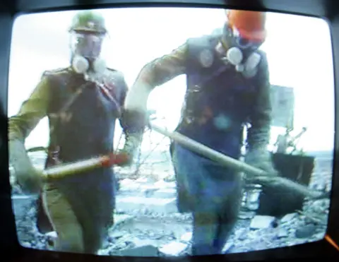 SERGEI SUPINSKY/AFP via Getty Images) A TV at the Chernobyl museum in Kiev shows a documentary film about the liquidators. Framed by the black edges of an old-style television set, the image shows two men in lead aprons, construction helmets and respirators carrying shovels.