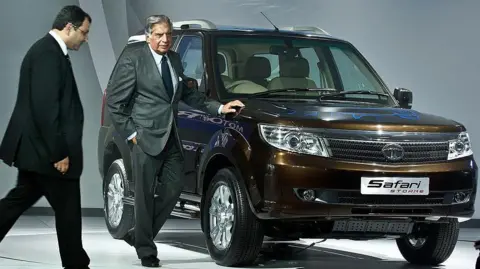 AFP via Getty Images Tata Group chairman Ratan Tata (R) looks on as Cyrus Mistry (L) walks past at the 2012 India Auto Expo in New Delhi on January 5, 2012. Behind them is a showroom model of the Tata Safari car. 