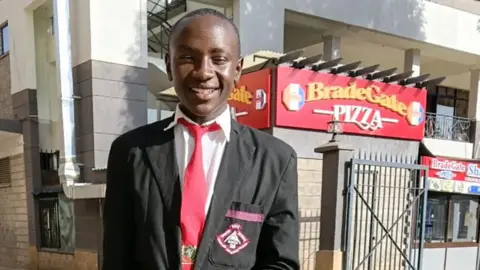 Family photograph A photograph of Sylvester Muigai Ndung'u in a school uniform. He is in a grey jacket, white shirt and red tie.