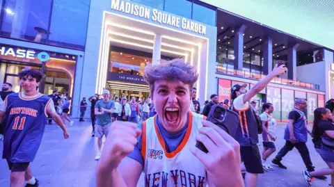 Getty Images A Knicks fan screaming in excitement in front of the camera as other fans surround him in front of Madison Square Garden