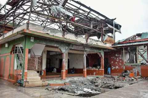 AFP via Getty Images A heavily damaged mosque, its roof almost entirely torn away and its steel framework twisted and exposed against a grey sky.