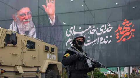 Getty Images A police officer stands near an armoured-vehicle and a poster featuring the late Supreme Leader Ali Khamenei on 28 March 2026 in Tehran, Iran.
