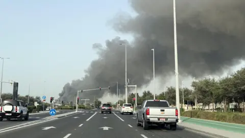 Reuters Several vehicles are seen on a multi-lane road in Abu Dhabi as smoke billows from Zayed port in the distance in the left of the picture