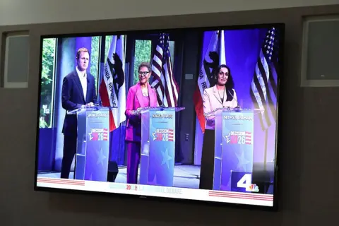 Getty Images A television screen shows Spencer Pratt, from left, Karen Bass and Nithya Raman taking part in the Los Angeles Mayoral debate at Skirball Cultural Center on 6 May 2026 in Los Angeles.
