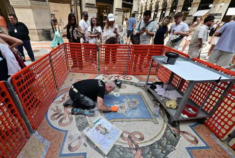 Stefano Rellandini/AFP via Getty Images Restorer Gianluca Galli works on the mosaic of the bull during the restoration in the Galleria Vittorio Emanuele II, in Milan on 28 May 2026. 