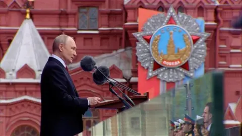 Kremlin.ru/Handout via Reuters Russian President Vladimir Putin stands wearing a dark suit at a lectern in Moscow's Red Square as he gives a speech.