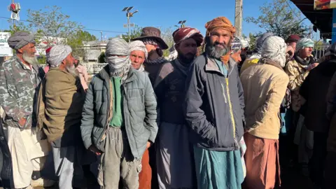 Imogen Anderson/BBC Men gather, some with their faces covered, hoping to get work early in the morning 
