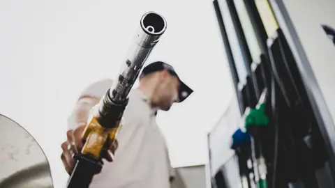 AFP via Getty Images A low-angle picture of a man holding a fuel pump at a petrol station