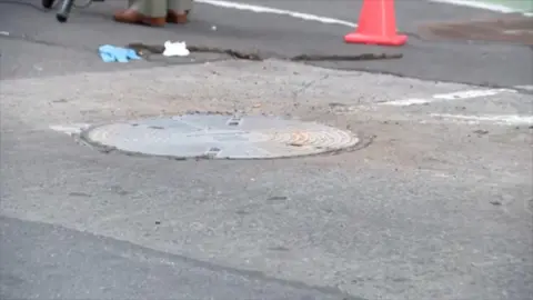 CBS A covered manhole on a street with an orange cone nearby 