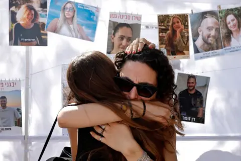 Reuters Two women hug in grief at the site of the Nova festival attack, on 7 October 2025