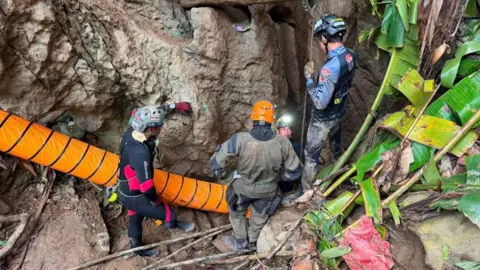 Reuters Four rescuers wearing helmets stand at the entrance to a cave