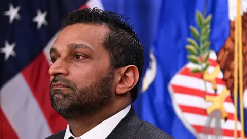 Getty A close-up photo of Kash Patel in profile standing in front of a flag. He is wearing a suit and tie, and his expression is solemn.