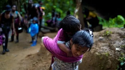 Reuters A migrant carries a child as she and others continue their journey to the US border, in Acandi, Colombia, 9 July 2023