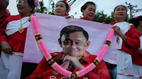Reuters Supporters of Thaksin Shinawatra, holding a banner with the former PM's face and a pink garland over it, wait for his release on parole after serving eight months of his one-year sentence at Klong Prem Central Prison in Bangkok