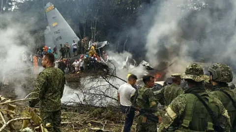Daniel Ortiz / AFP via Getty Image Soldiers and rescuers are seen near an Air Force Hercules plane from which thick smoke is rising after the aircraft crashed during take-off in Puerto Leguizamo, Colombia(Photo by daniel ortiz / AFP via Getty Images)