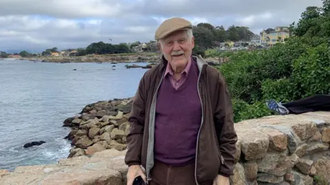 Submitted photo Arthur Rose stands in front of the ocean, wearing a purple sweater, brown jacket and cap