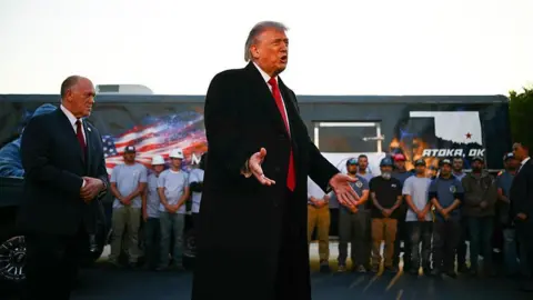 AFP via Getty Images Trump speaking in front of a line of workers in front of a work truck