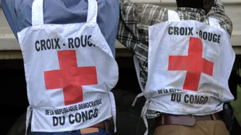 AFP via Getty Images Two individuals are pictured from behind wearing Red Cross tabards.The tabards read