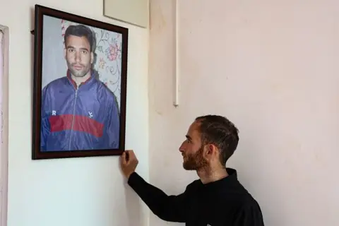 Getty Images Nazakat looks at a portrait of his brother Adil Shah, who was killed during an incident in Pahalgam last year, at his new home in Hapatnar, Pahalgam, Jammu and Kashmir, India, on April 21, 2026. (Photo by Nasir Kachroo/NurPhoto via Getty Images)