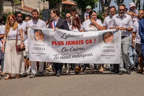 AFP via Getty Images People carry a large banner featuring a picture of Lyhanna with the words, "We'll never forget you" and "Lyhanna, never again! We love you. We miss you", during a march in Fleurance on 7 June.