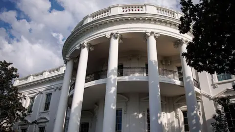Getty Images The exterior of the White House in Washtington DC is seen from a low angle and between trees.
