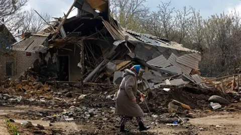 Reuters An elderly woman walks past the ruins of a house in Donetsk