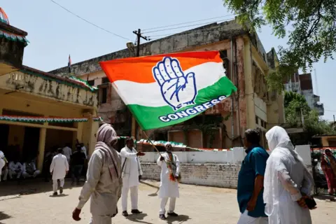 Reuters Man waves a large flag with the word "Congress" written on while several people walk past him