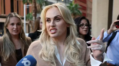 Reuters A woman with long blonde hair and wearing a light brown jumper and white shirt, speaking and gesturing with her hand