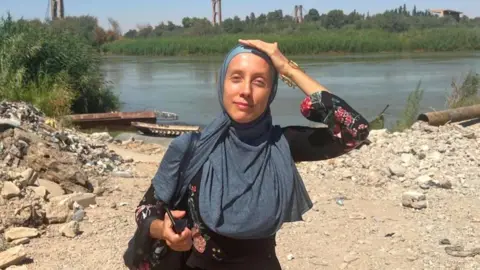 Shelly Kittleson/X An undated image of Shelly Kittleson. She wears a hijab and holds a phone while standing in front of a river
