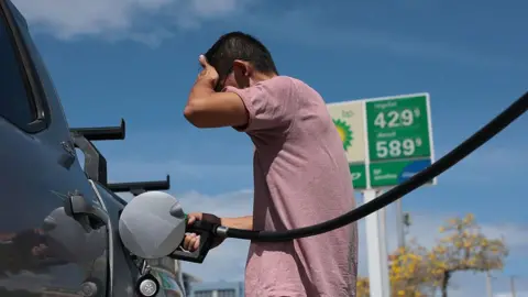 Getty Images A man palms his forehead in frustration while filling his truck up with gasoline. 