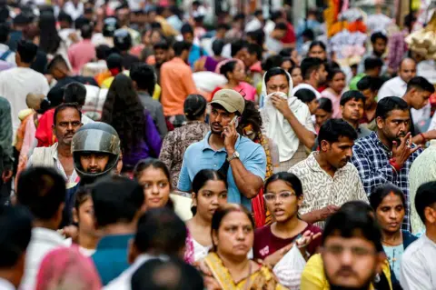 AFP via Getty Images A man speaks on a mobile phone as he walks across a crowded market in Varanasi