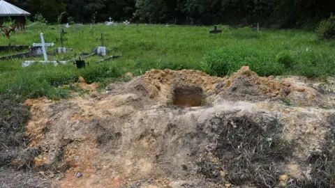 AFP via Getty Images An open grave at the site in Cumuto, the rest of which shows graves with crosses on overgrown grass