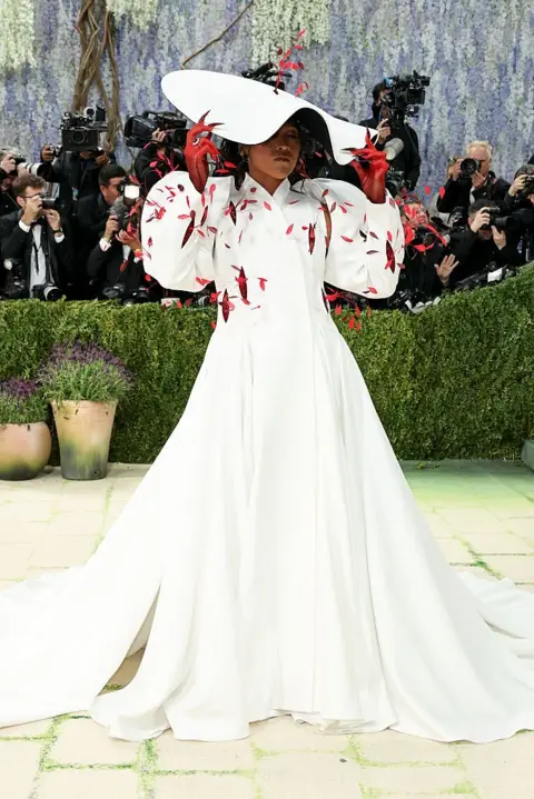 Getty Images Naomi Osaka wears a white coat dress and dramatic white hat.