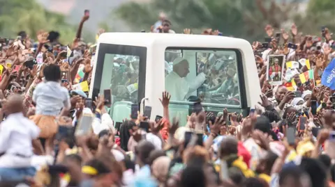 AFP via Getty Images Crowds surrounding Pope Leo's white vehicle after he landed in Yaoundé, Cameroon