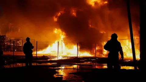 Reuters Two rescuers are silhouetted against a backdrop of fire in Kyiv