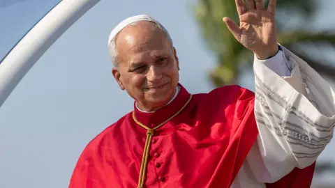 EPA/Shutterstock Pope Leo waves as he arrives in Angola. He has white hair and wears red and white robes.