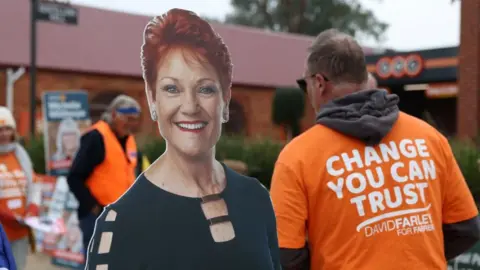 Reuters A cardboard cutout of Pauline Hanson on the left with a man in an orange campaign t-shirt on the right in front of a polling station.