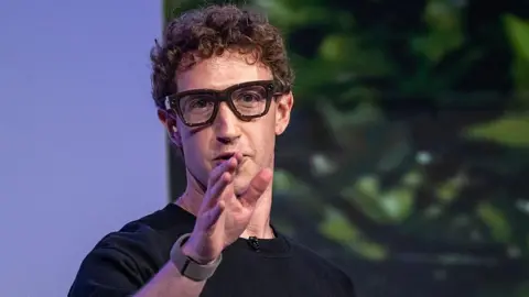 Getty Images Mark Zuckerberg wearing thick black rimmed smart glasses and gesturing with his hand.