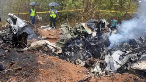 Reuters Two people with umbrellas and high-viz jackets are seen at the wreckage of the aircraft in Kwale County, Kenya
